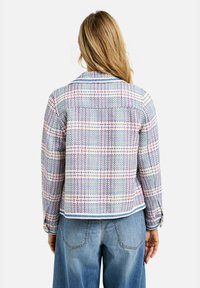 Mehrfarbige karierte Jacke aus strukturiertem Stoff, mit Kragen, blauen Akzenten und Manschetten. Das Design umfasst horizontale und vertikale Linien.