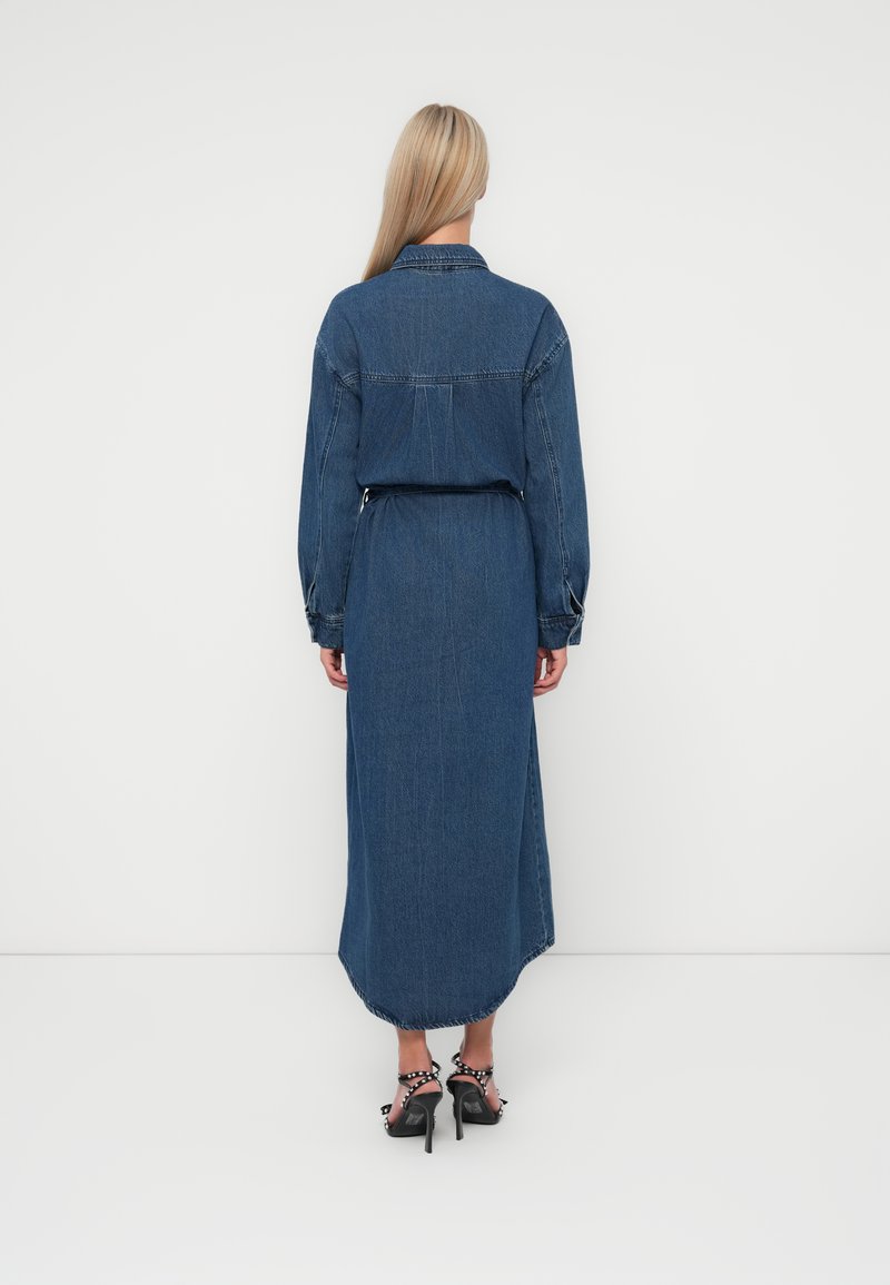 Sukienka koszulowa z denimu w ciemnoniebieskim kolorze, z długim rękawem i spiczastym kołnierzykiem, dopasowana w talii, z lekko płynącą sylwetką w kształcie litery A, z rozciętym dołem.