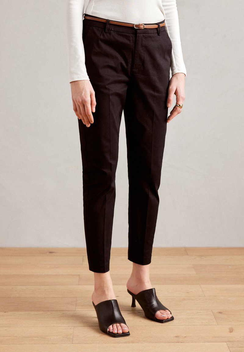 Zwarte maatwerk broek met een slim fit en een vouw, gecombineerd met zwarte open teen muilen. Voorzien van een bruine leren riem. Glad textuur, minimalistisch ontwerp.