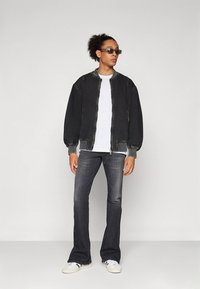 Juoda bombonešio striukė su ribotomis rankogaliais, balti marškinėliai, tamsūs džinsai ir balti sportbačiai. Stilius yra laisvas ir patogus.