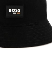Zwarte stoffen bucket hat met gestikte details. Bevat een rechthoekig logo-opdruk met "BOSS" in witte, zwarte en gouden letters.