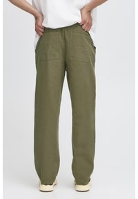 Olivengrønne bomuldsbukser med en afslappet pasform, der har to baglommer og en glat tekstur, kombineret med lyse sko.