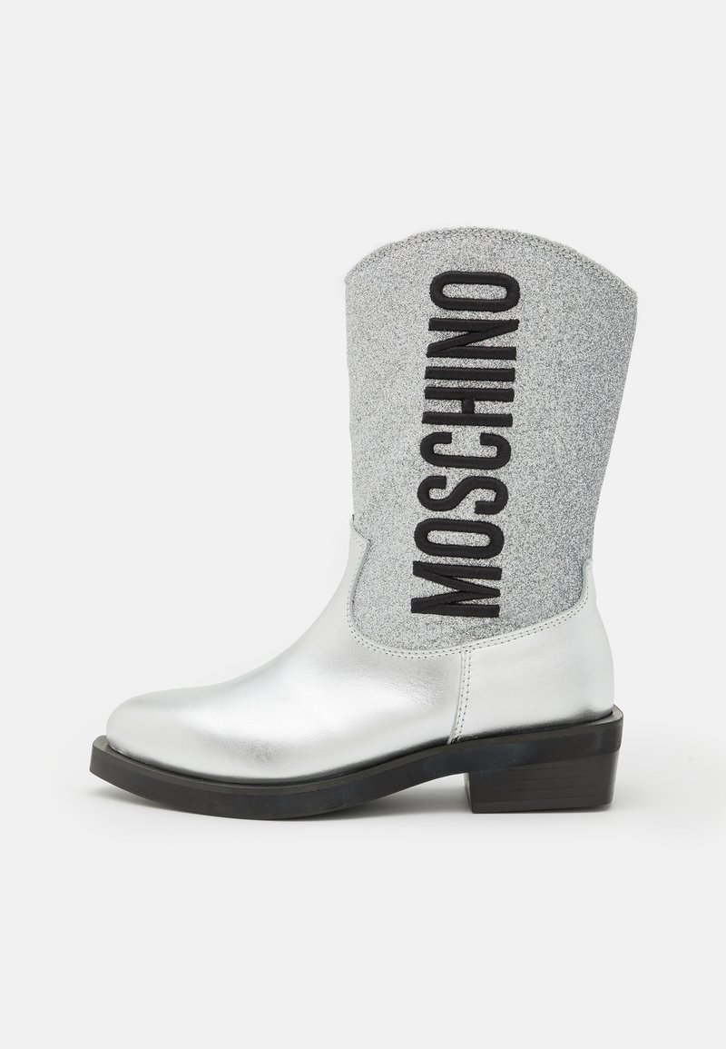 Bottine en métal argenté avec un revers pailleté gris portant "MOSCHINO" en lettres noires bold ; petit talon carré et texture lisse.