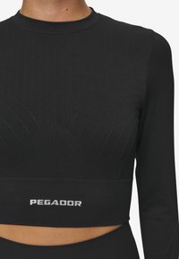 Fekete, hosszú ujjú crop top, bordázott textúrával és kerek nyakkivágással. Emelt mintázatú részletek és "PEGADOR" logó található az alján.