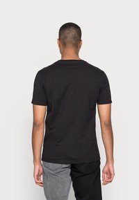 Camiseta de algodón negra, de manga corta, cuello redondo, diseño sencillo, textura suave, entallada en los hombros, costuras visibles, combinada con pantalones grises y negros.