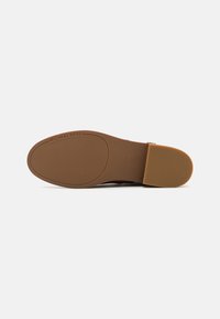 Semelle d'une chaussure Michael Kors marron avec une adhérence texturée et la taille 7M indiquée, présentée sur un fond clair uni.