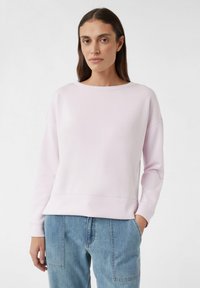 Jasnoróżowy sweter wykonany z miękkiego materiału, z okrągłym dekoltem, opadającymi ramionami i ściągaczami na rękawach, zestawiony z niebieskimi dżinsami.