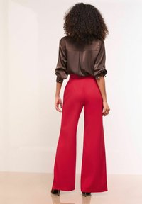 Barna selyem blúz feltekert ujjakkal és hátsó varrással, magasan derekú piros, széles szárú nadrággal párosítva, sima textúrát bemutatva.