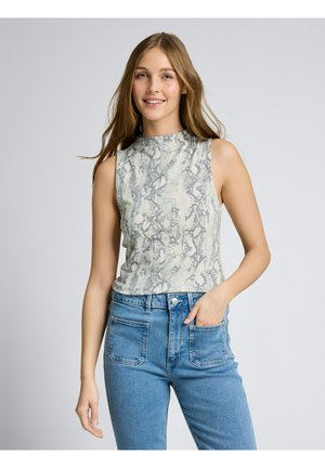 Giovane donna sorridente, con indosso un top grigio senza maniche con motivo a serpente e jeans blu a vita alta, con una mano in tasca.