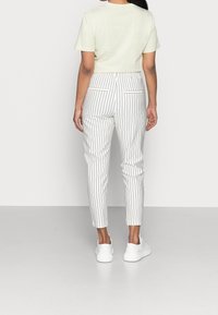 Valkoiset raidalliset housut slim fit -mallilla, joissa on kaksi takataskua, yhdistetty vaaleanvihreään lyhytvartiseen t-paitaan ja valkoisiin tennareihin.