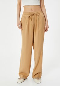 Lichtbeige wijde broek gemaakt van soepele stof met een elastische tailleband en trekkoord. Voorzien van zijzakken en een ontspannen pasvorm.