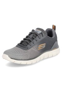 Scarpa atletica grigia con tomaia in rete, accenti arancioni a contrasto, punta arrotondata e suola bianca leggera; presenta un design con lacci e un colletto imbottito.