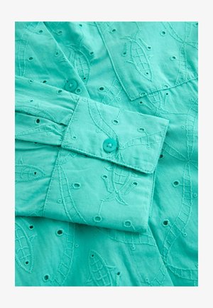 Turkis bomuldsbluse med broderede fisk og svungne mønstre, udstyret med knapmanchetter og små udskæringer.