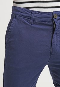 Námořnické modré kalhoty vyrobené z bavlněné směsi. Mají rovný střih, přední kapsy a zapínání na zip s knoflíkovým uzávěrem.