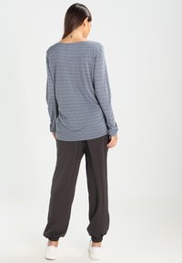 Långärmad marinblå topp med ett vitt diamantmönster, kombinerad med mörka smala byxor. Tygerna verkar mjuka med elastiska muddar på byxorna.