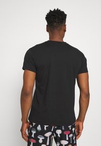 Black short-sleeve t-shirt with a crew neck, fitted design, and smooth texture. Worn with patterned pants featuring various mushrooms.