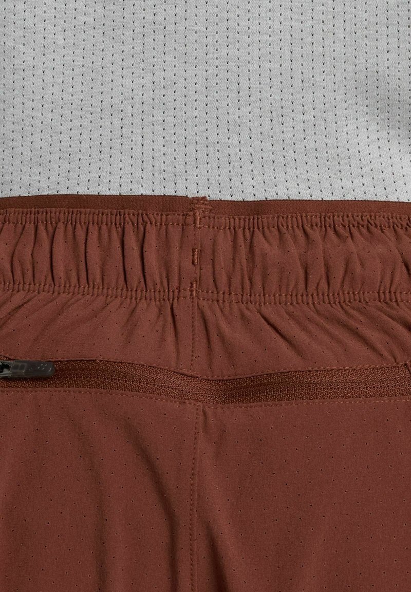 Bordeauxrode korte broek met een elastische tailleband, voorzien van kleine perforaties voor ventilatie en een gladde stoftextuur.