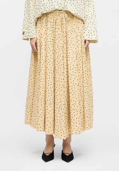 Μπεζ πλισέ μίντι φούστα με μαύρα πουά, συνδυασμένη με ένα μπλούζα με πουά στο ίδιο σχέδιο και μαύρες γόβες με μυτερή μύτη.