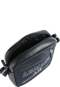 Borsa a tracolla sintetica blu con dettagli in pelle nera, tasca anteriore con zip, logo "ARMANI" e tracolla regolabile a righe. Scomparto principale con zip.