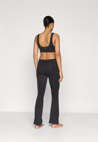 Top desportivo preto com alças largas e costas baixas, combinado com leggings pretos flare. Material liso com design ajustado.