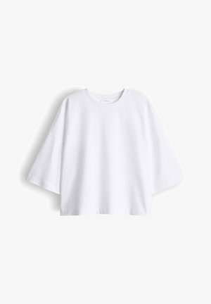 T-shirt blanc surdimensionné à manches courtes avec un col rond, une coupe ample et des coutures d'épaule tombantes sur un fond uni.