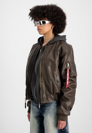 Brown leather bomber jacket with a zip closure, ribbed cuffs, and pocket details; paired with a grey hoodie and denim jeans. White sunglasses.