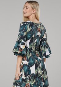 Kleid mit Blumenmuster und kurzen, Rüschensleeves; die vorherrschenden Farben sind dunkelgrün, weiß und rot; mit taillierter Passform und lebhaften Blattmustern.