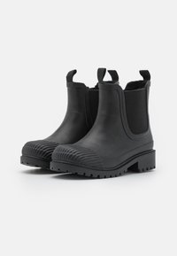 Bottes noires en caoutchouc à la cheville avec un design épuré, des panneaux latéraux élastiques et un capuchon de orteil texturé. Elles possèdent une semelle robuste à crampons pour une meilleure adhérence.