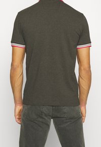 Polo gris foncé à manches courtes, avec des accents rayés rose et gris sur le col et les manches. Texture lisse, coupe standard.