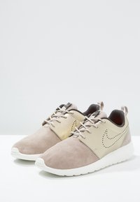 Beige suede and metallic gold sneakers with round toe, textured upper, and white rubber sole; features lace-up closure and perforated accents.