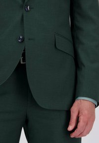 Donkergroen colbertsak met twee knopen, een borstzak en bijpassende broek. Kenmerkt zich door een lichtblauwe voering aan de mouwen en een gladde textuur.