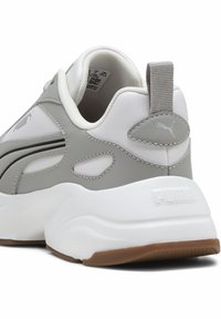 Sneaker grigia e bianca con tomaia in materiale sintetico, accenti testurizzati, intersuola bianca imbottita e suola in gomma naturale marrone. Presenta il dettaglio del logo Puma.