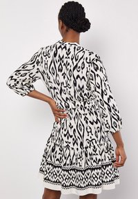 Schwarz-weißer gemusterter Kleid mit langen Ärmeln, einem gestuften Rock und einer taillierten Taille. Hergestellt aus leichtem Stoff mit glatter Textur.
