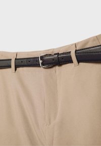 Gros plan sur un pantalon beige avec une ceinture en cuir noire passée dans les passants et une boucle argentée.