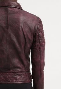 Giacca in pelle bordeaux con un design trapuntato sulle spalle e finitura testurizzata, dotata di vita con cintura e silhouette aderente.