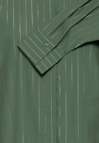 Grün gestreiftes Hemd mit vertikalen weißen Linien, Knopfmanschette, glatte Textur und taillierte Passform, die das schlanke Design betont.