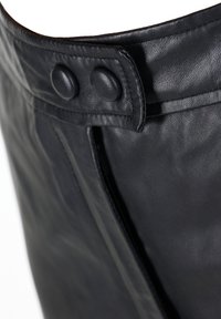 Schwarze Lederhandtasche mit glatter Oberfläche, abgerundetem Oberrand und zwei auffälligen Knöpfen am Verschluss. Enthält einen Reißverschluss an der Seite.