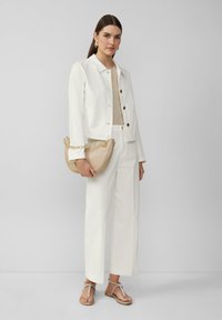 White jacket with button closure, beige top, and white wide-leg pants. Tan handbag with chain strap and flat sandals with knot detail.