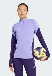 Light purple zip-up sports top with dark purple long sleeves, paired with matching pants. The model holds a black and yellow soccer ball.