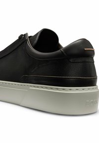 Black leather sneaker with a textured finish, a slim silhouette, and a light-colored rubber sole. Features minimalist silver hardware accents.