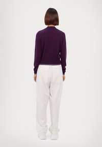 Pull en maille violet à encolure arrondie, vue de dos. Associé à un pantalon blanc à fines rayures, ample, pour un style décontracté.