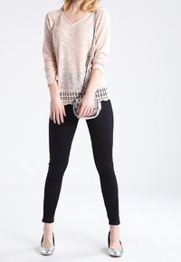 Ljusrosa långärmad topp med texturerat mönster och spetsdetaljer, tillsammans med svarta slim-fit byxor och silverfärgade klackar. Liten metallisk crossbody-väska.
