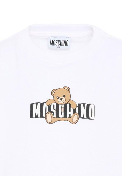 T-shirt blanc pour enfants avec une illustration d'ourson en peluche serrant le nom de la marque "MOSCHINO" en noir et blanc sur la poitrine.