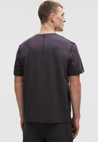 Kratký rukáv, tmavě šedé sportovní tričko s kulatým výstřihem, hladká textura, ploché švy a decentní detail na zádech poblíž krku.