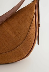 Bolso de ante color canela con forma curva, correa de cuero, patrón de diamantes en relieve y detalles de costuras a lo largo de los bordes. Textura suave.