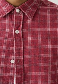 Rotes karierte Flanellhemd mit einem Kragen zum Knöpfen, weißen Knöpfen und einer weichen Textur mit weißen und blauen Akzenten im Muster.