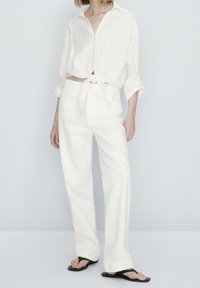 Witte crop top met een strik in de taille, gecombineerd met losse witte broeken en zwarte slippers. Gladde textuur, minimalistisch ontwerp.