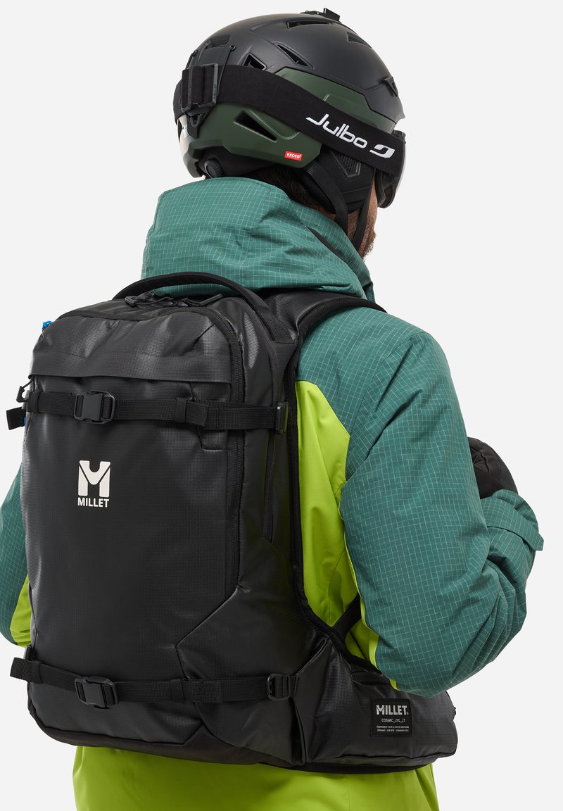 Czarny plecak z prosa z regulowanymi paskami, teksturowanym wykończeniem i logo. Nosi się go na zielonej i limonkowej kurtce w kratę.