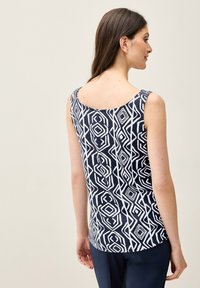 Ärmlös marinblå topp med ett geometriskt vitt mönster, båtutskärning och texturerade axelremmar. Slät tygkvalitet med avslappnad passform.