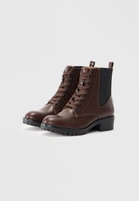 Bottes chelsea en cuir marron avec un laçage à l'avant, bout rond, semelle en caoutchouc texturé et panneaux latéraux élastiques pour un enfilage facile.